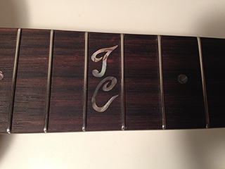 Close up view of abalone inlayed initials in rosewood fingerboard